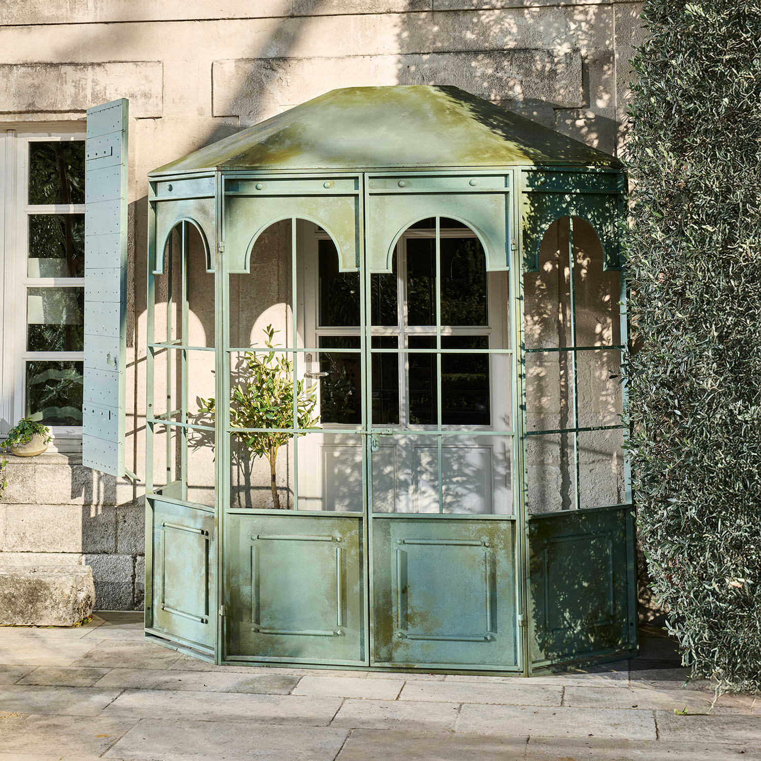 Kiosque de jardin en métal vert avec panneaux vitrés et arches décoratives sur terrasse en pierre