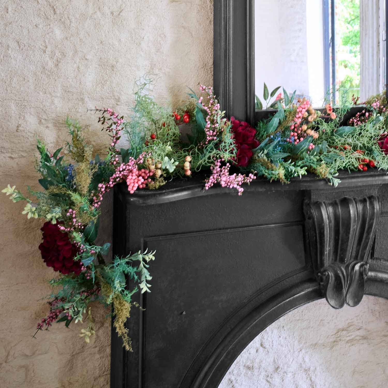 Guirlande décorative avec baies rouges et roses et feuillage vert sur une cheminée noire