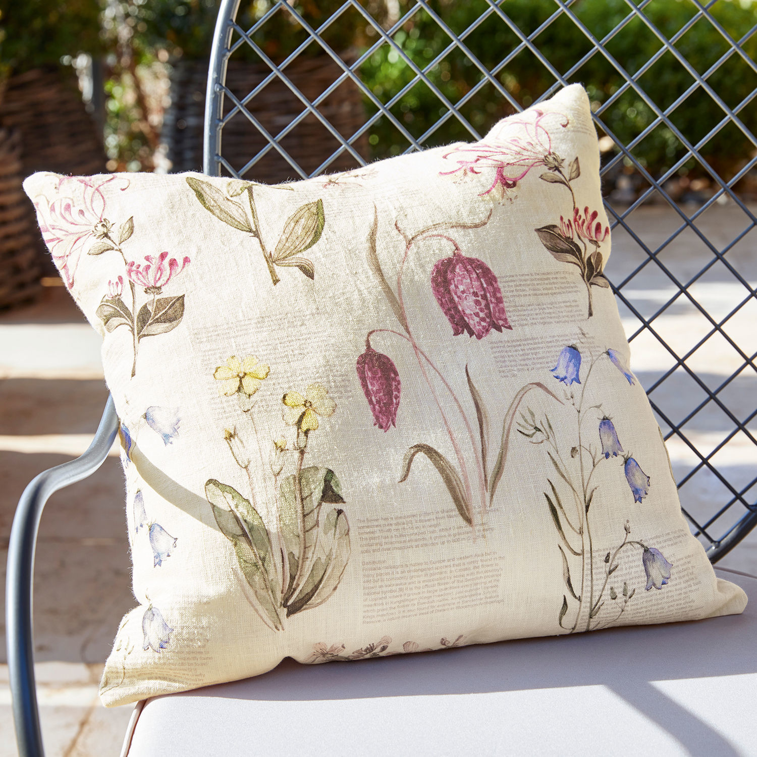 Housse de coussin Fournier Coussin en lin beige avec imprimé floral vintage posé sur une chaise de jardin