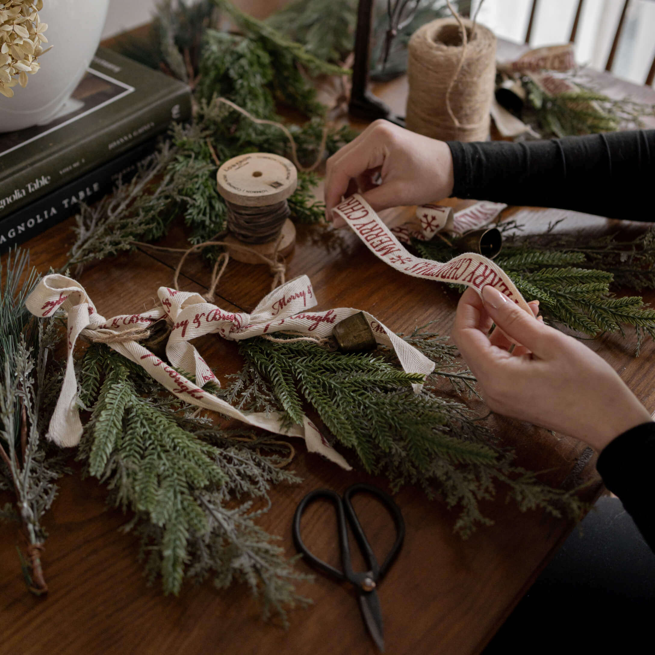 Mains décorant des branches de sapin avec un ruban en coton Merry Christmas sur une table en bois avec des ciseaux