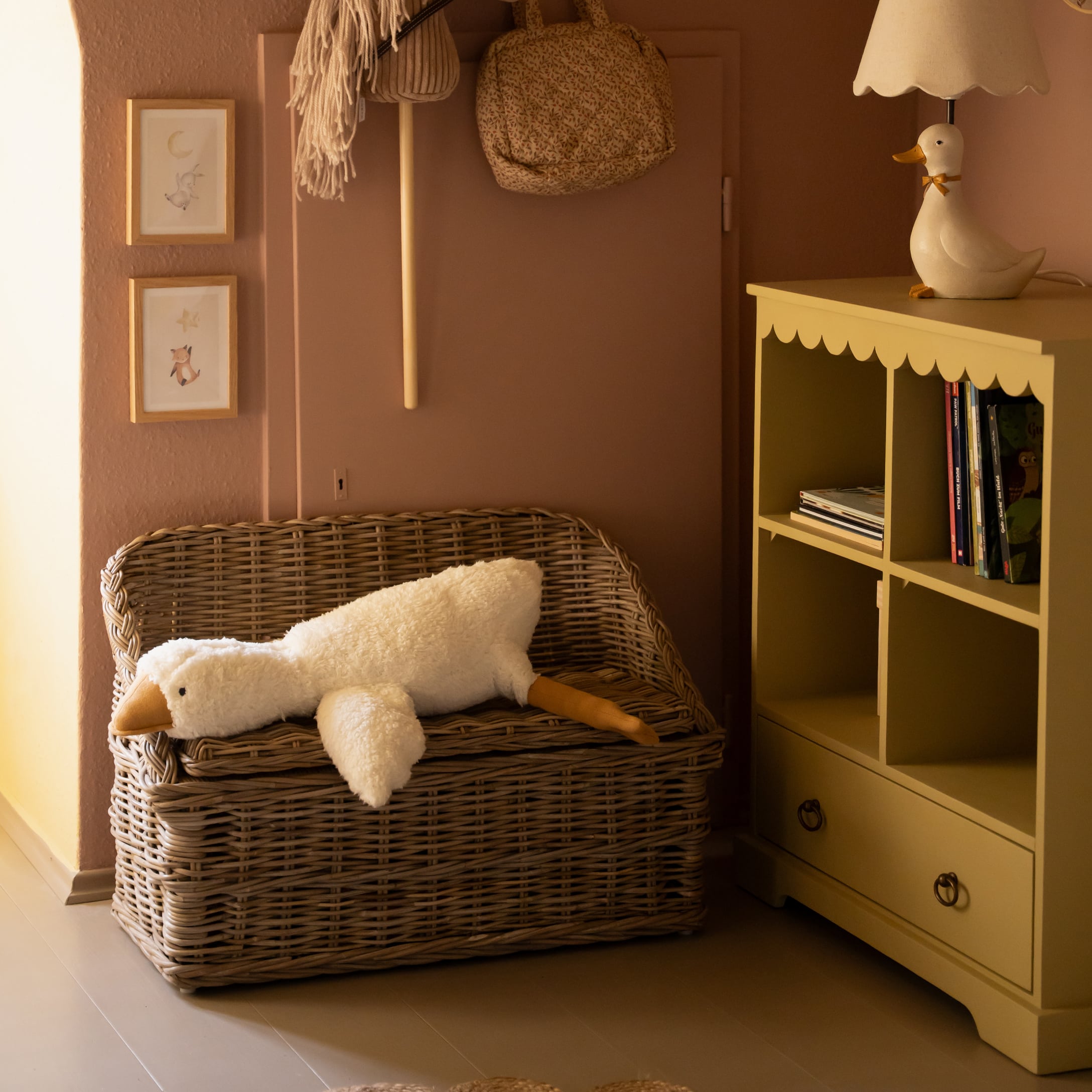 Banc en osier avec peluche blanche en forme de canard allongé dans une chambre d'enfant chaleureuse
