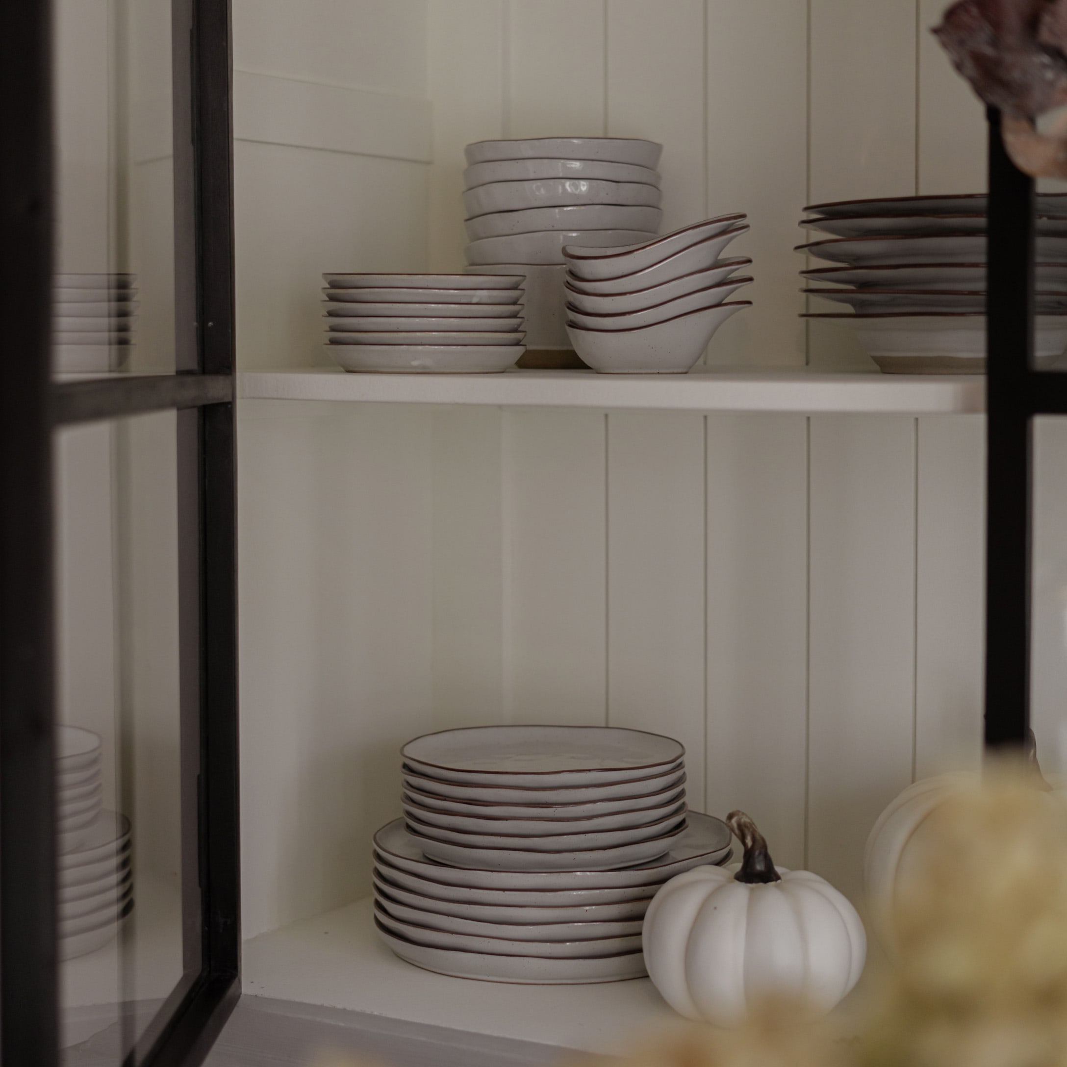 Ensemble de vaisselle en céramique blanche avec bord brun sur étagère, citrouille blanche décorative à côté