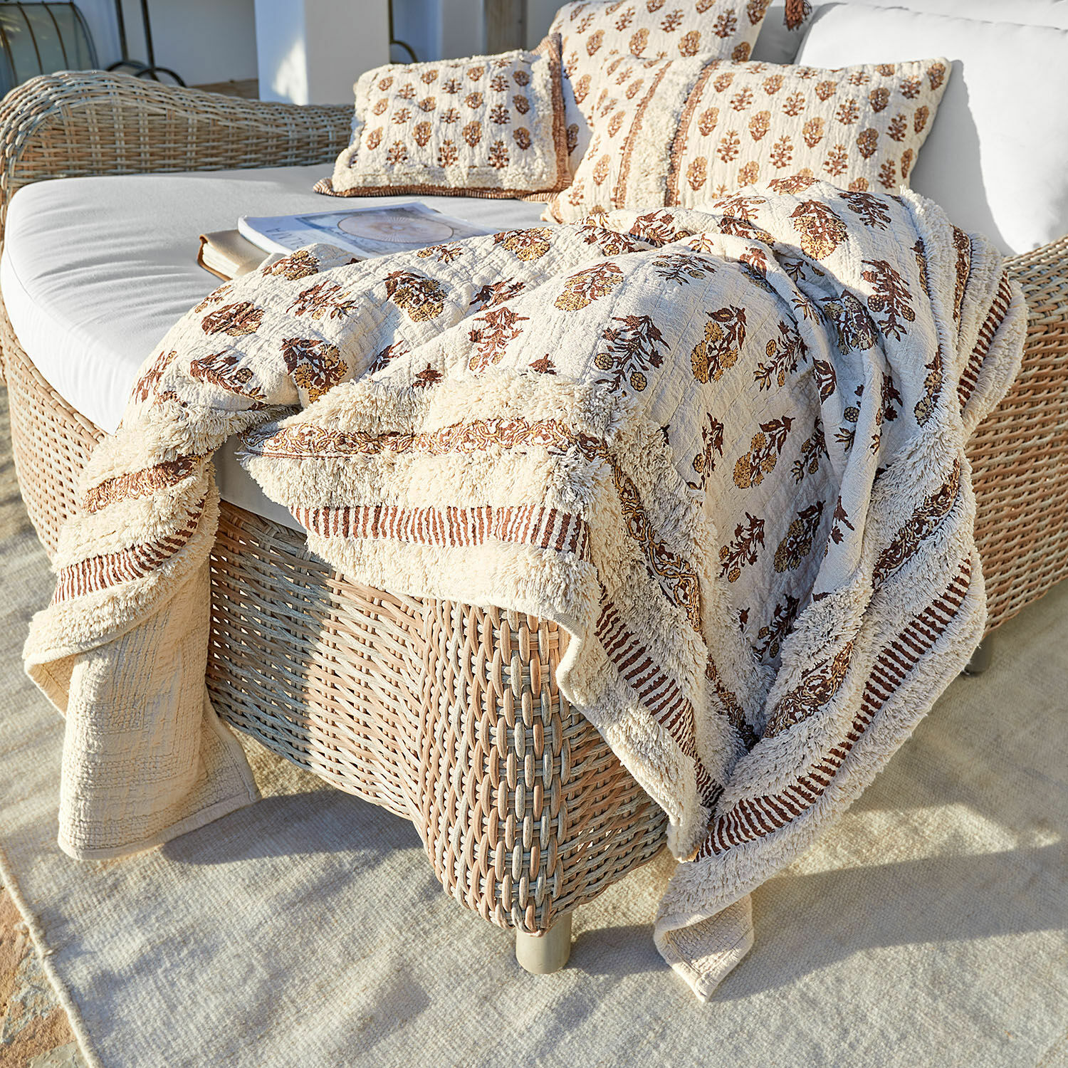 Plaid Arsalan Plaid et coussins en coton beige avec motif marron sur canapé en osier en terrasse