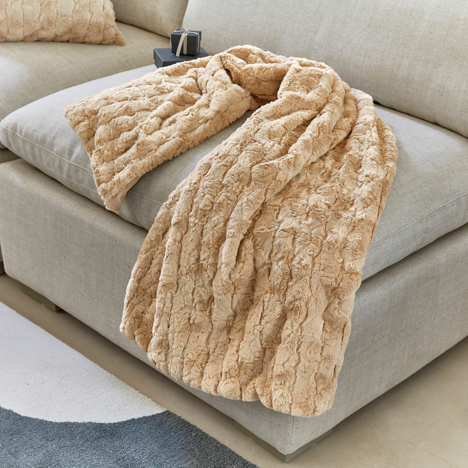 Plaid Dorelice Plaid beige en fausse fourrure posé sur un canapé gris clair pour un intérieur cosy