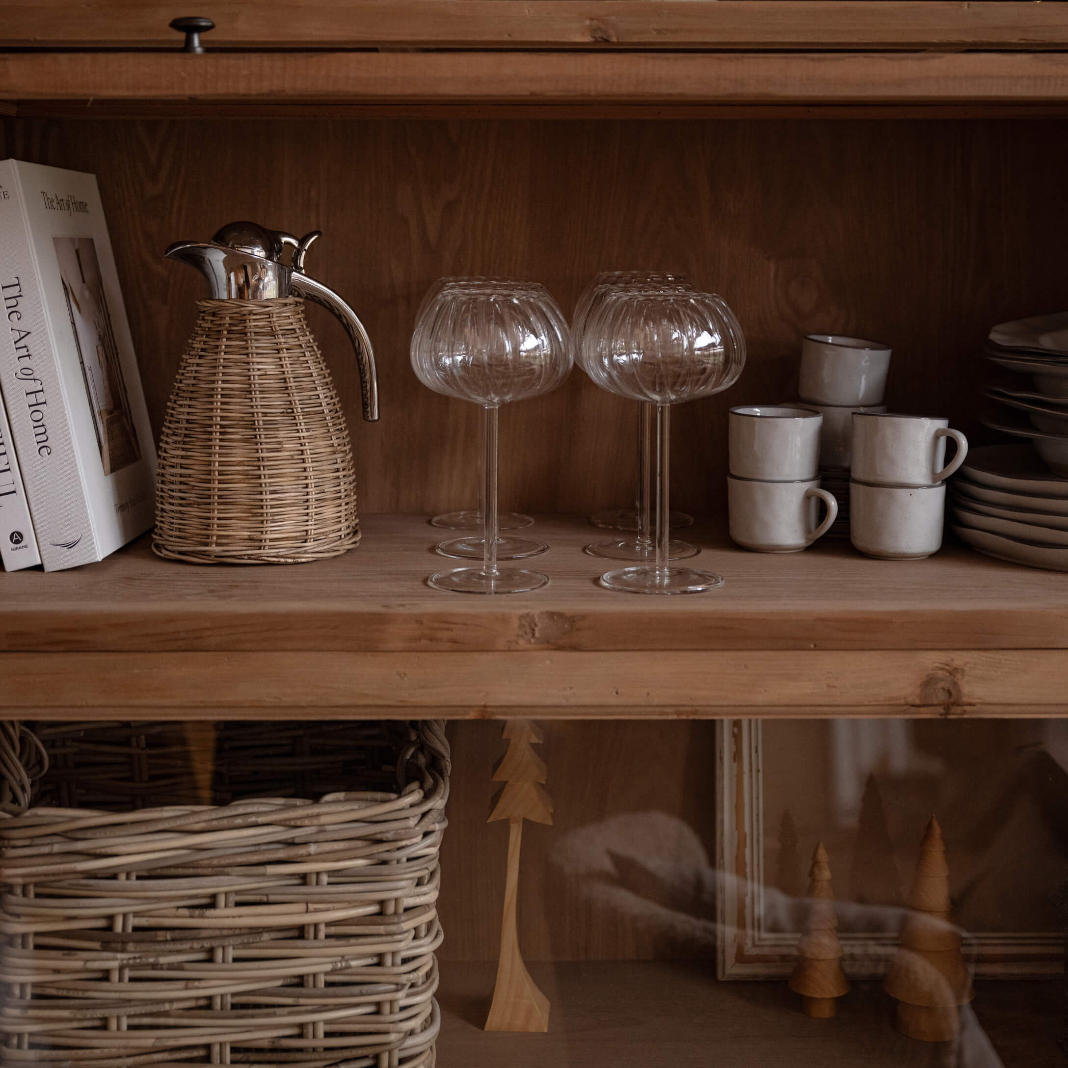 Verres en verre gravé sur étagère en bois avec pichet en osier et tasses blanches empilées