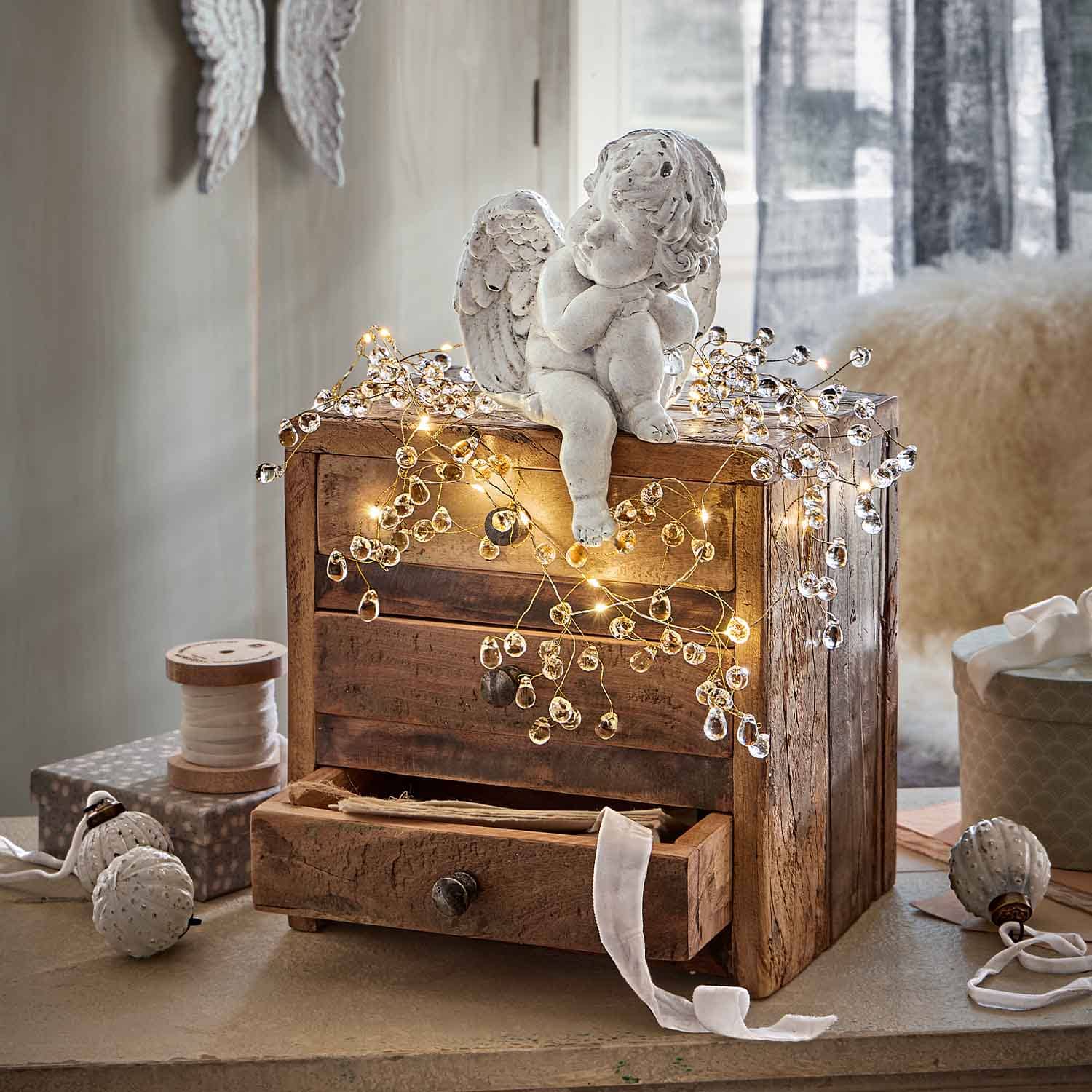 Figurine d'ange en céramique blanche posée sur un coffre en bois décoré de guirlandes lumineuses LED chaudes