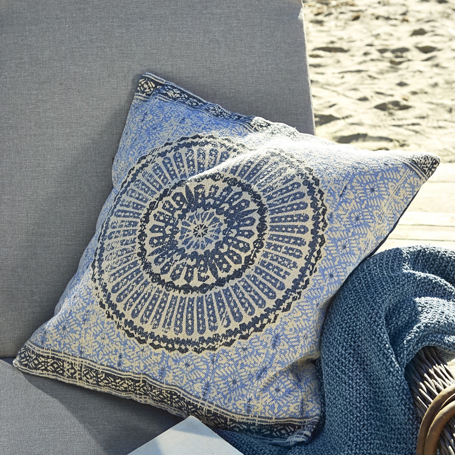 Coussin Kelcie Coussin décoratif en coton bleu et beige avec motif oriental posé sur un canapé gris