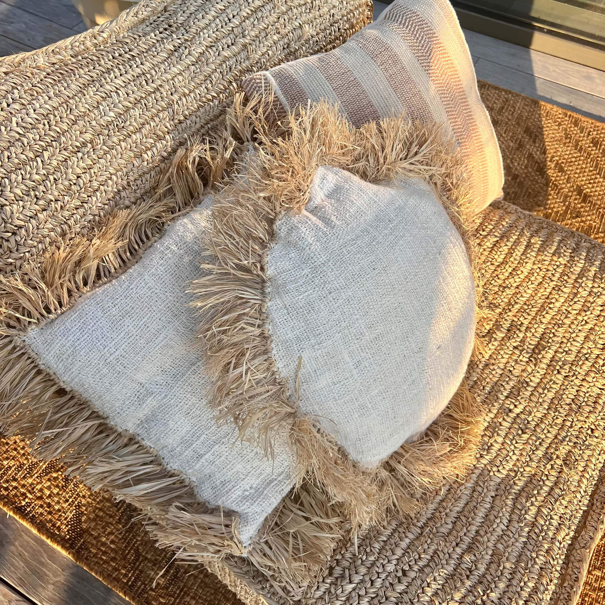 Coussins décoratifs en matière naturelle beige posés sur un fauteuil en jute tressée pour salon extérieur