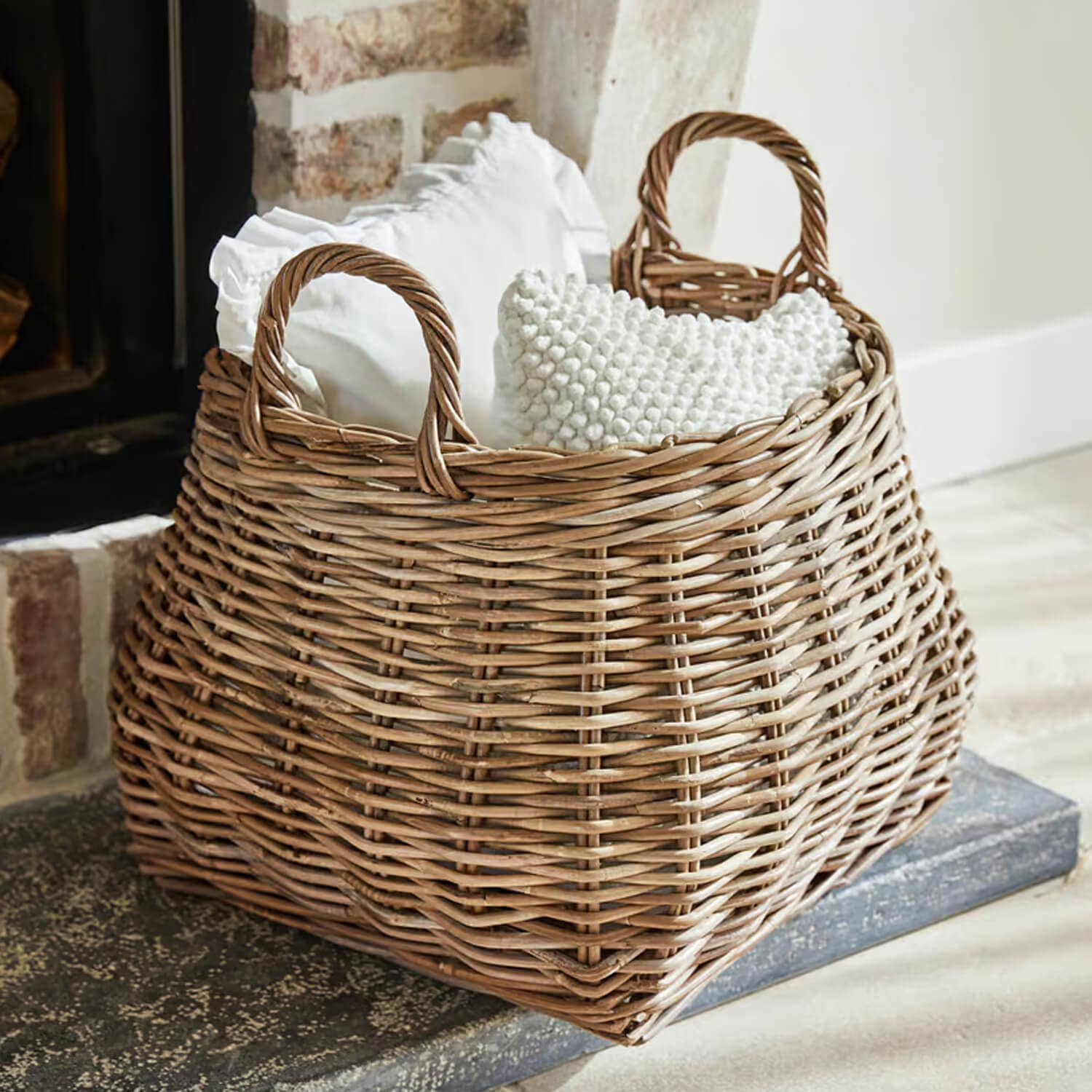 Panier en osier naturel avec poignées, rempli de coussins blancs, idéal pour rangement et décoration intérieure
