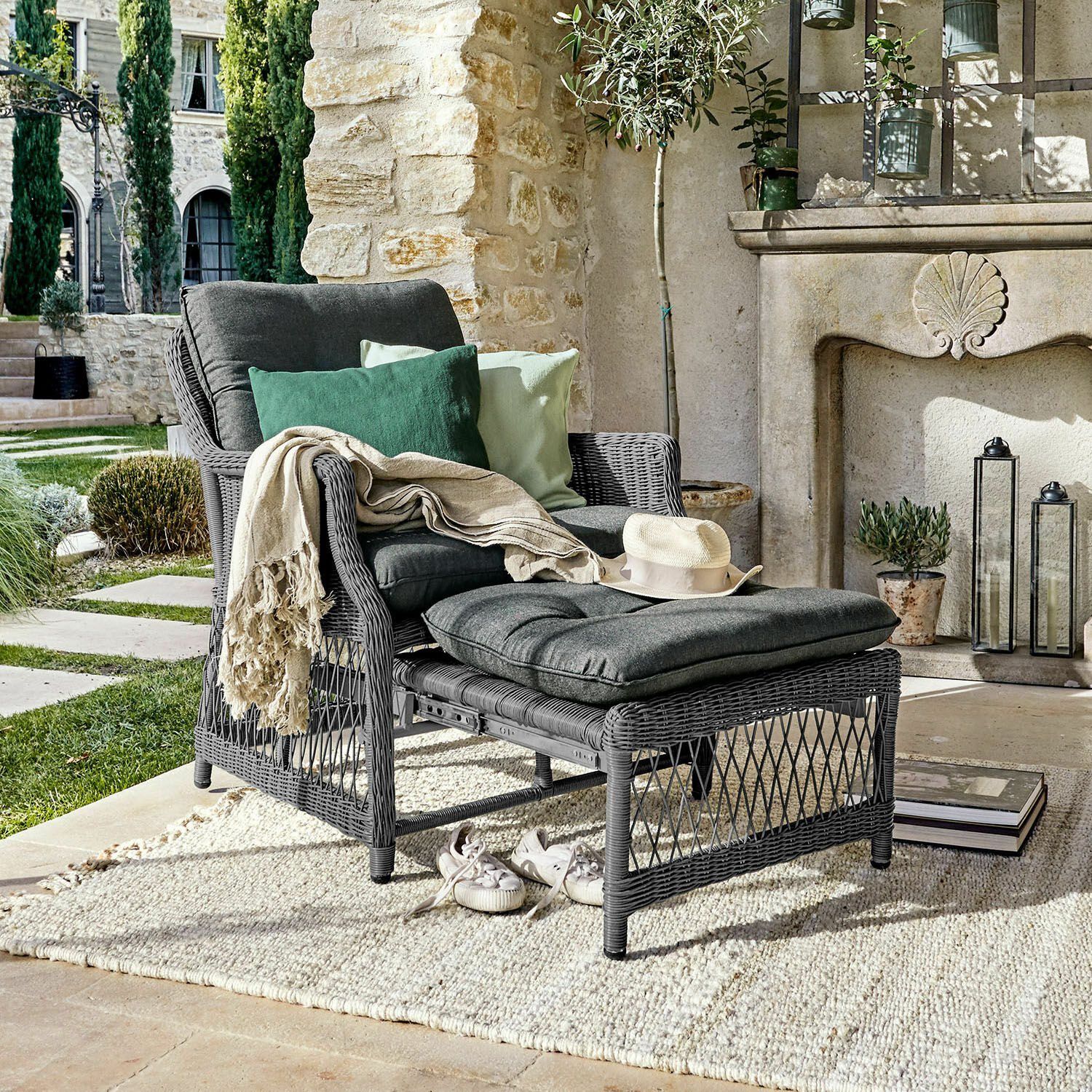 Fauteuil Howe Fauteuil en rotin gris avec repose-pieds et coussins gris foncé, décoré de coussins verts sur une terrasse extérieure