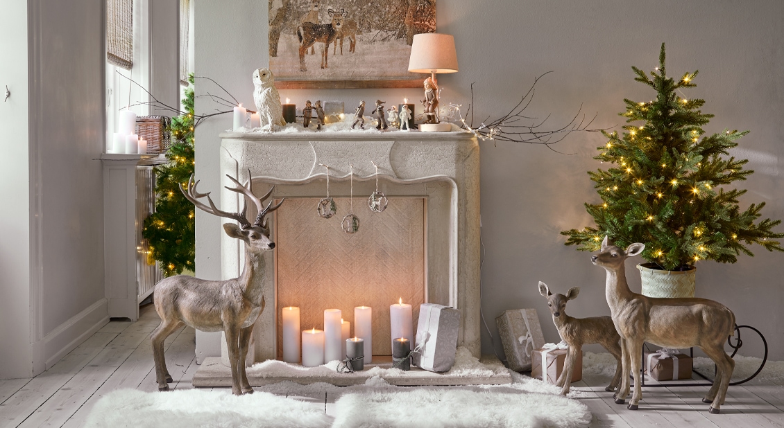 Console de cheminée en pierre blanche avec décorations de Noël et figurines de cerfs dans un intérieur chaleureux