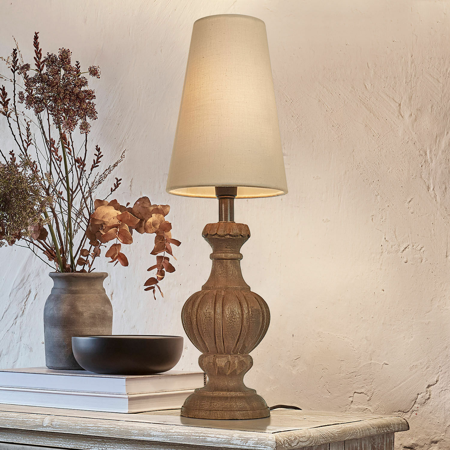 Lampe de table avec base en bois sculpté et abat-jour crème sur une table rustique décorée