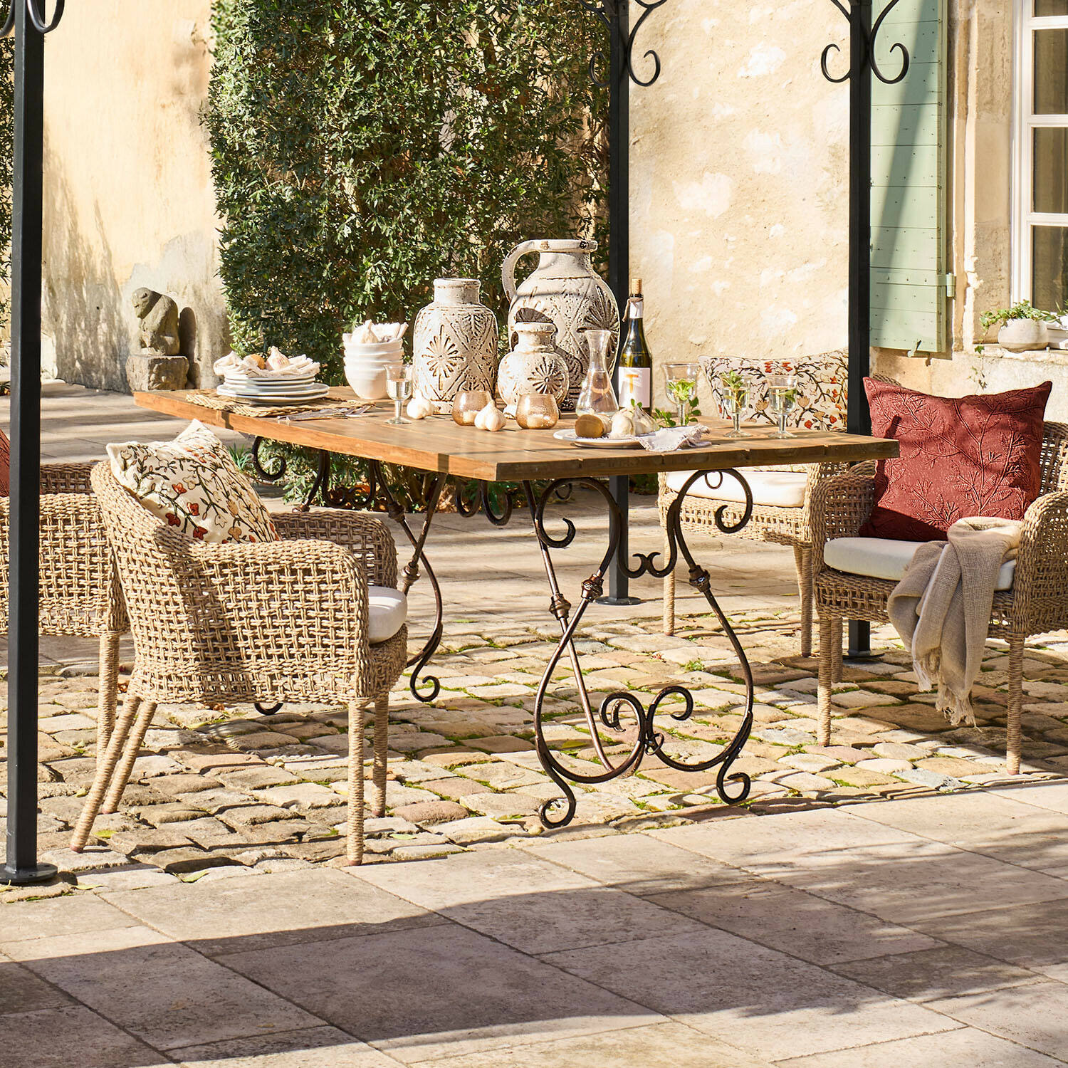 Table de jardin en bois avec pieds en métal et chaises en osier avec coussins et décorations en céramique