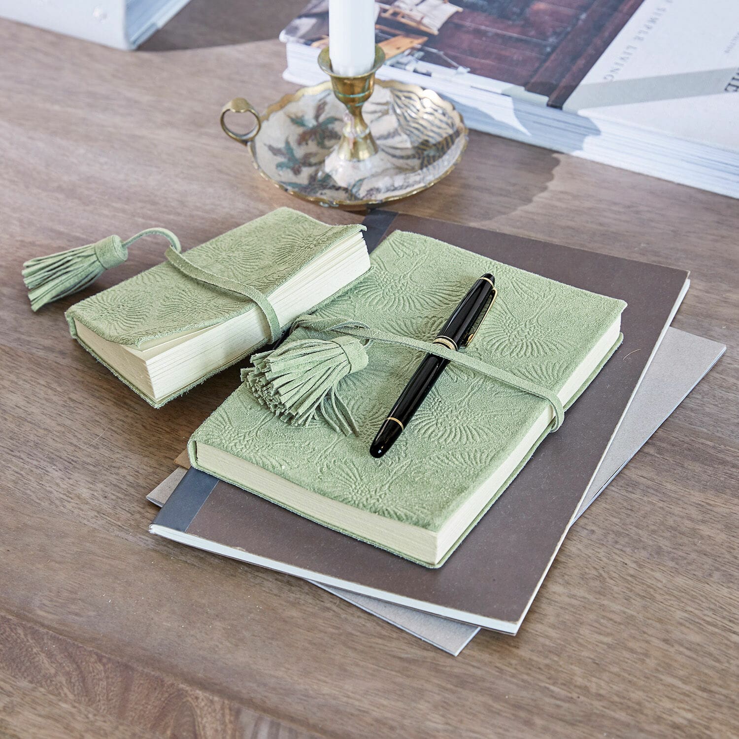 Lot de 2 calepins Houdain Carnet vert en cuir souple embossé avec pompons posé sur un bureau en bois avec stylo noir