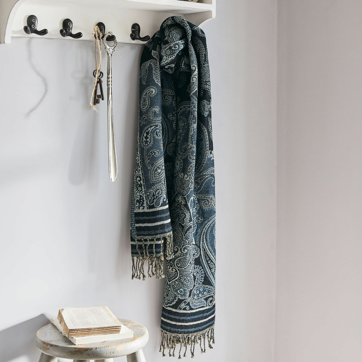 Étole Eloas Écharpe bleu marine à motif paisley avec franges suspendue à un porte-manteau blanc dans un intérieur clair