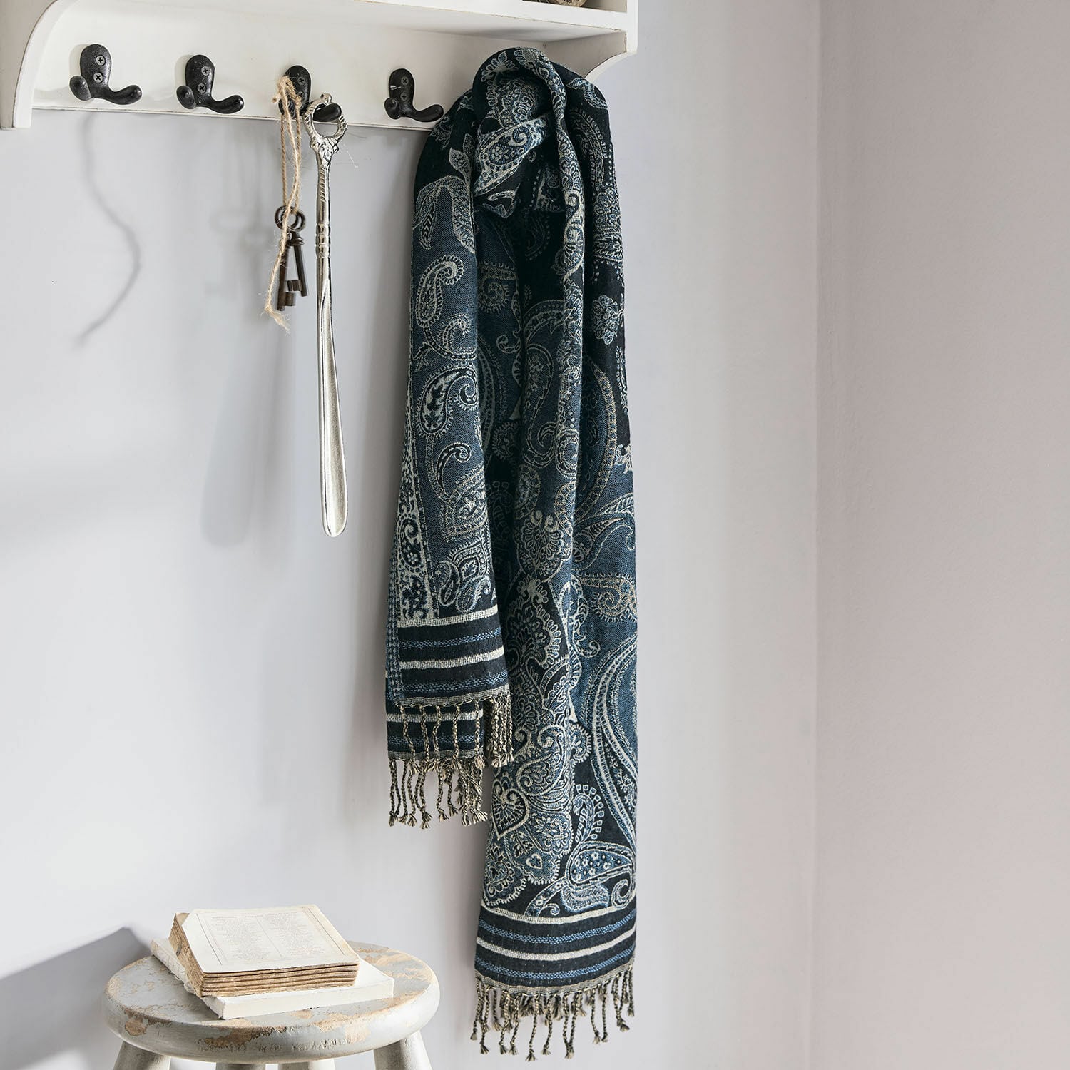 Étole Eloas Écharpe bleu marine à motif paisley avec franges suspendue à un porte-manteau blanc dans un intérieur clair
