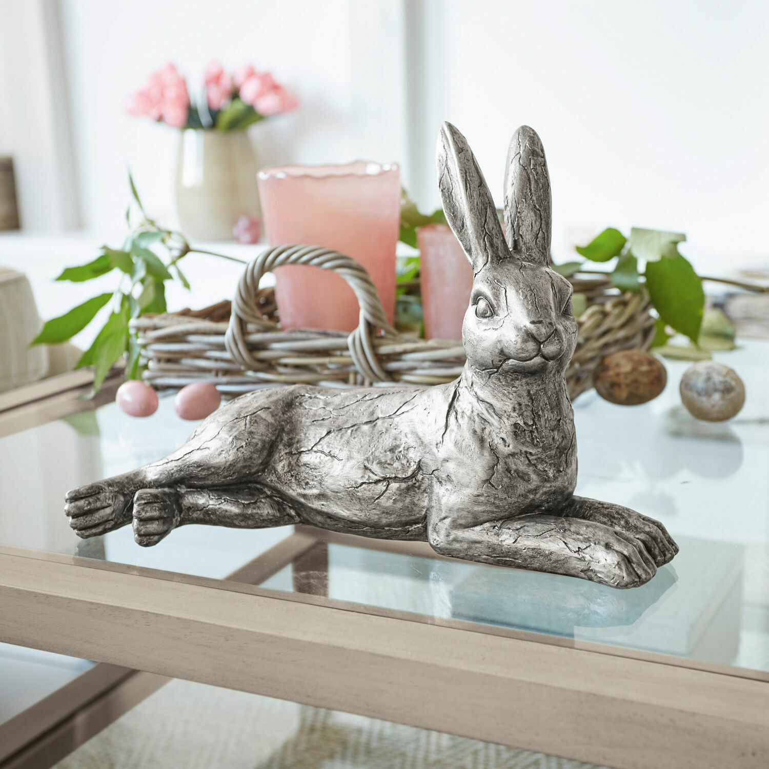 Lapin Fiorentin Lapin décoratif en métal argenté posé sur une table en verre avec décoration printanière