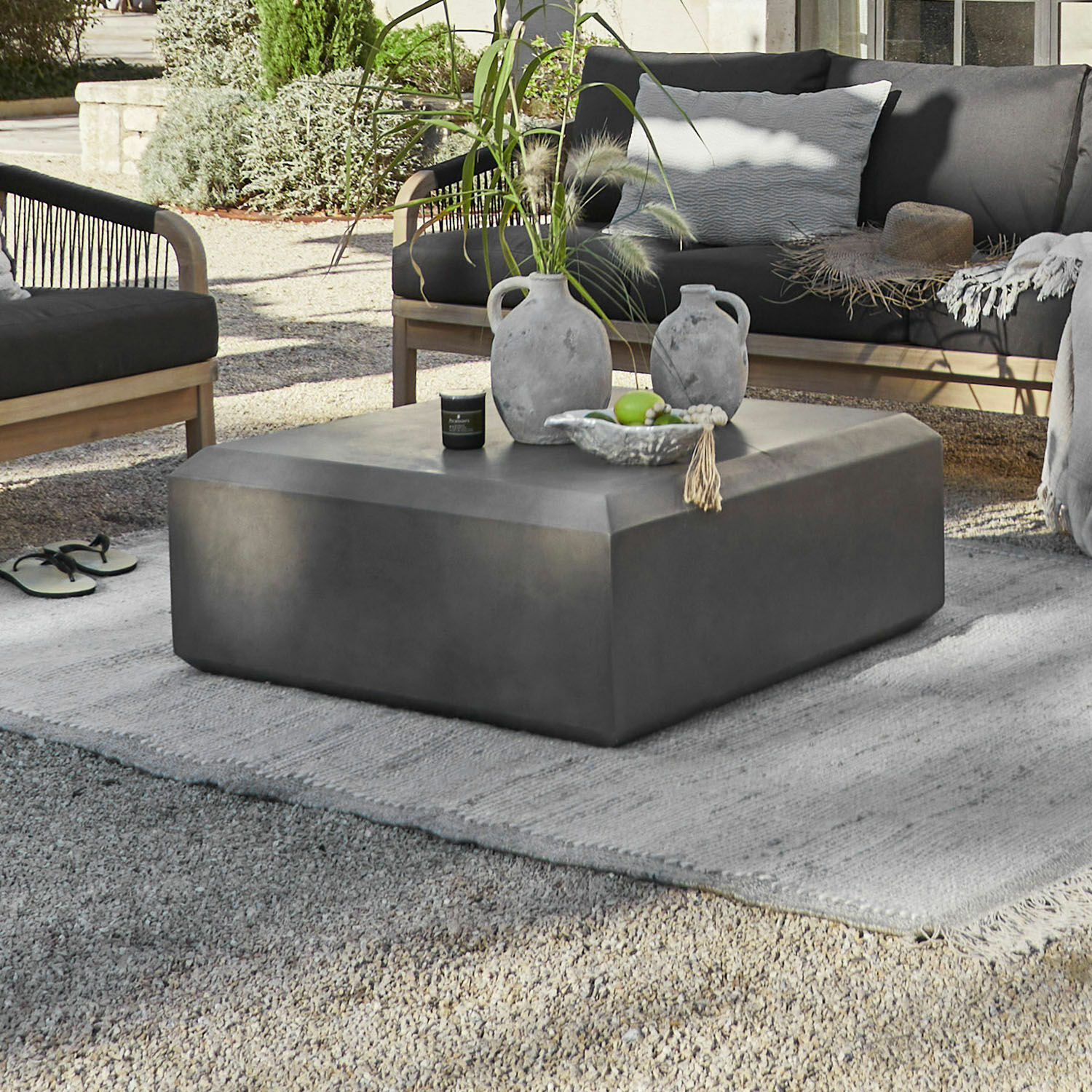 Table basse Theodoros Table basse moderne en béton gris dans un jardin avec décorations et mobilier extérieur