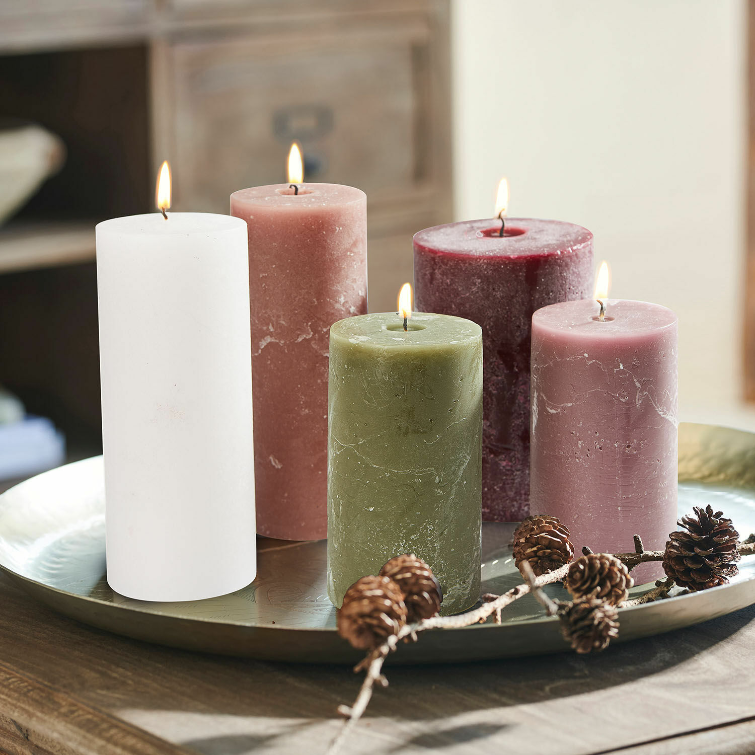 Lot de 5 bougies Panagra Ensemble de cinq bougies en cire de différentes couleurs sur un plateau en métal avec décoration de pommes de pin