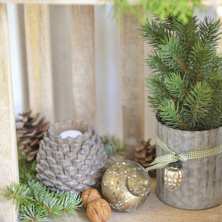 Bougeoir en forme de pomme de pin avec branches vertes dans un pot en métal sur une étagère en bois