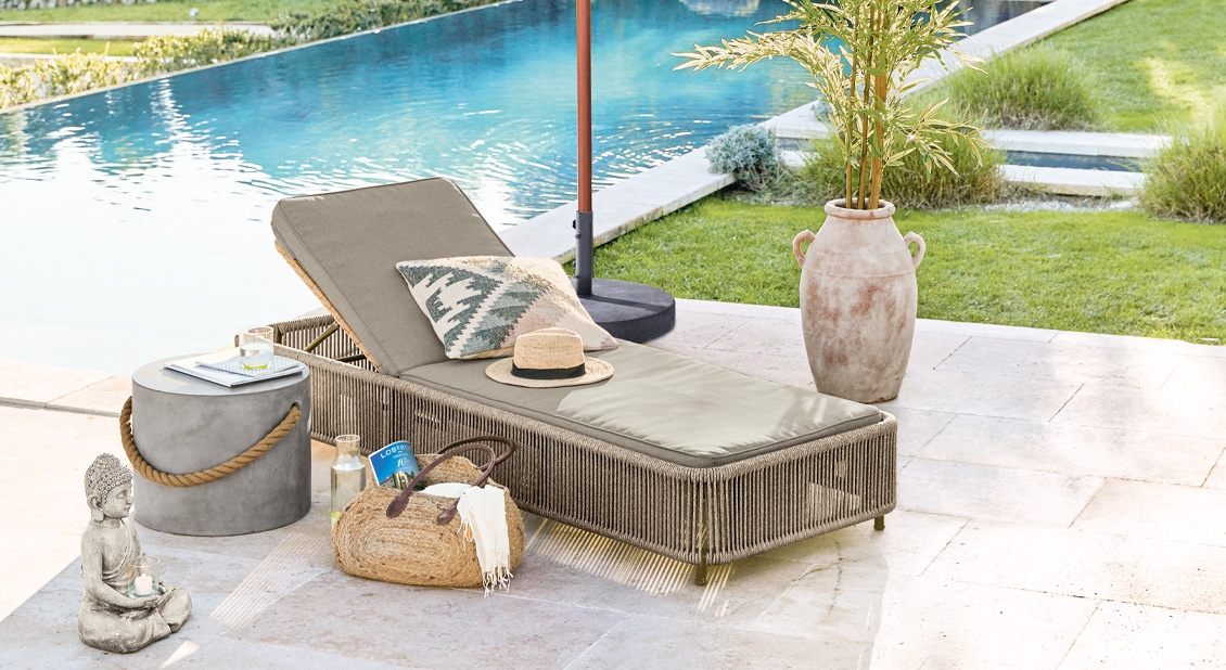Chaise longue de jardin beige avec coussin décoratif au bord de la piscine sur une terrasse en pierre claire