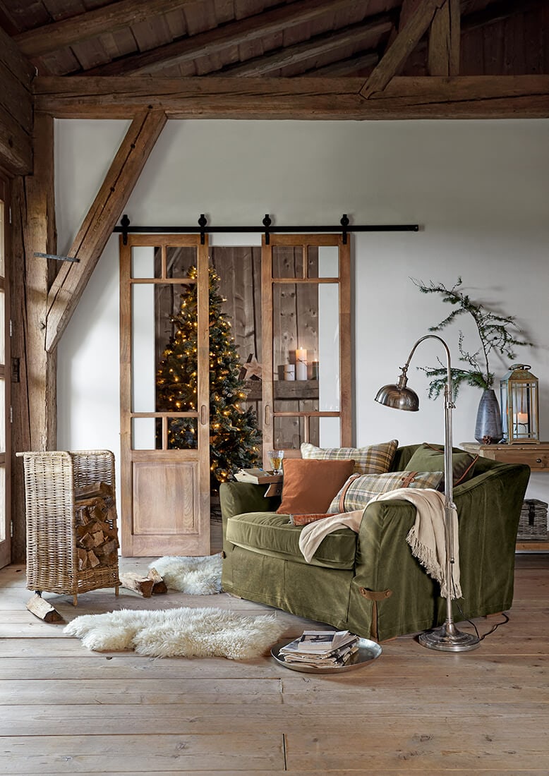Salon chaleureux avec canapé vert, portes coulissantes en bois et sapin de Noël décoré en arrière-plan