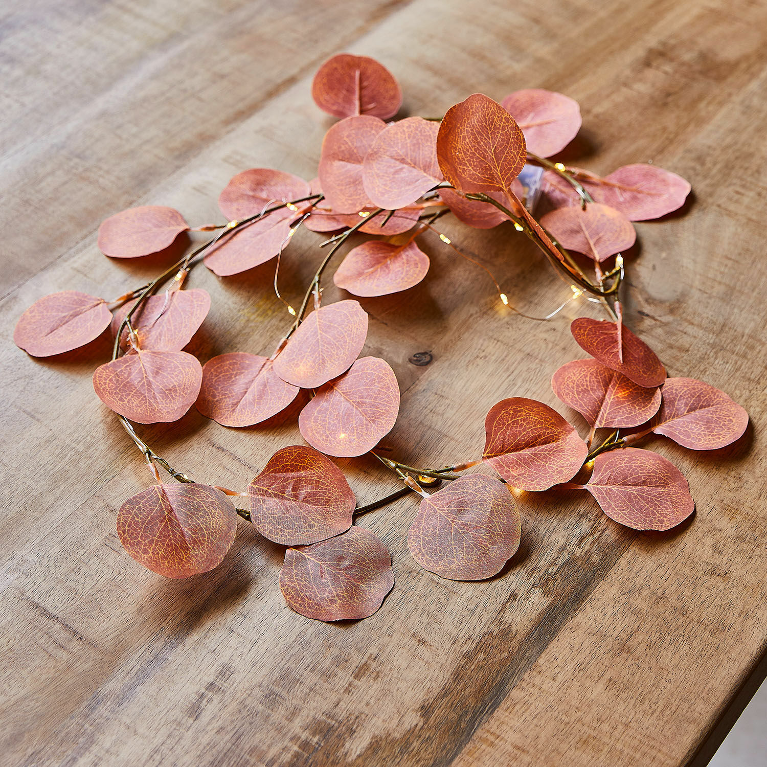 Guirlande lumineuse Gracielle Couronne décorative avec feuilles roses et petites lumières LED sur une table en bois