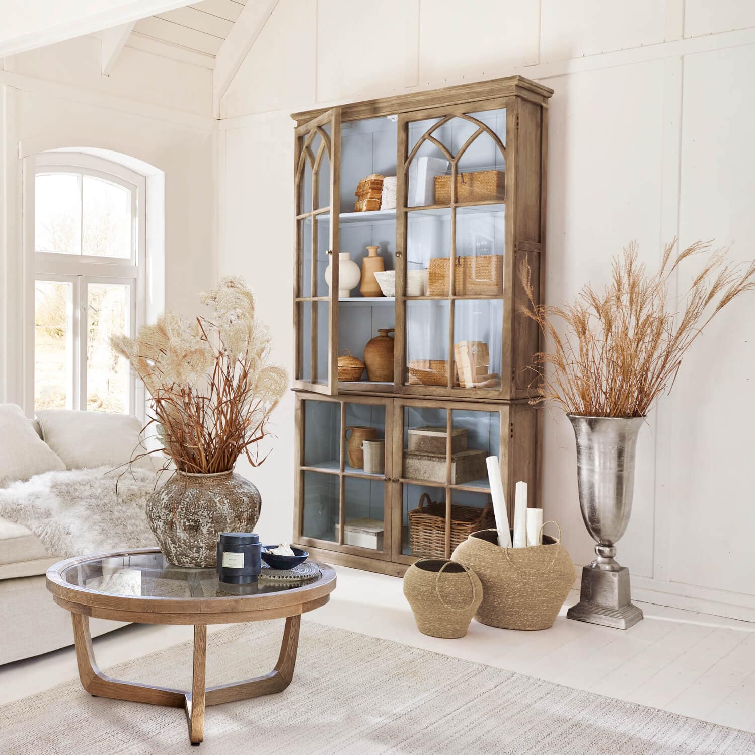 Salon chaleureux avec vitrine en bois, table en verre et décorations naturelles dans des tons clairs