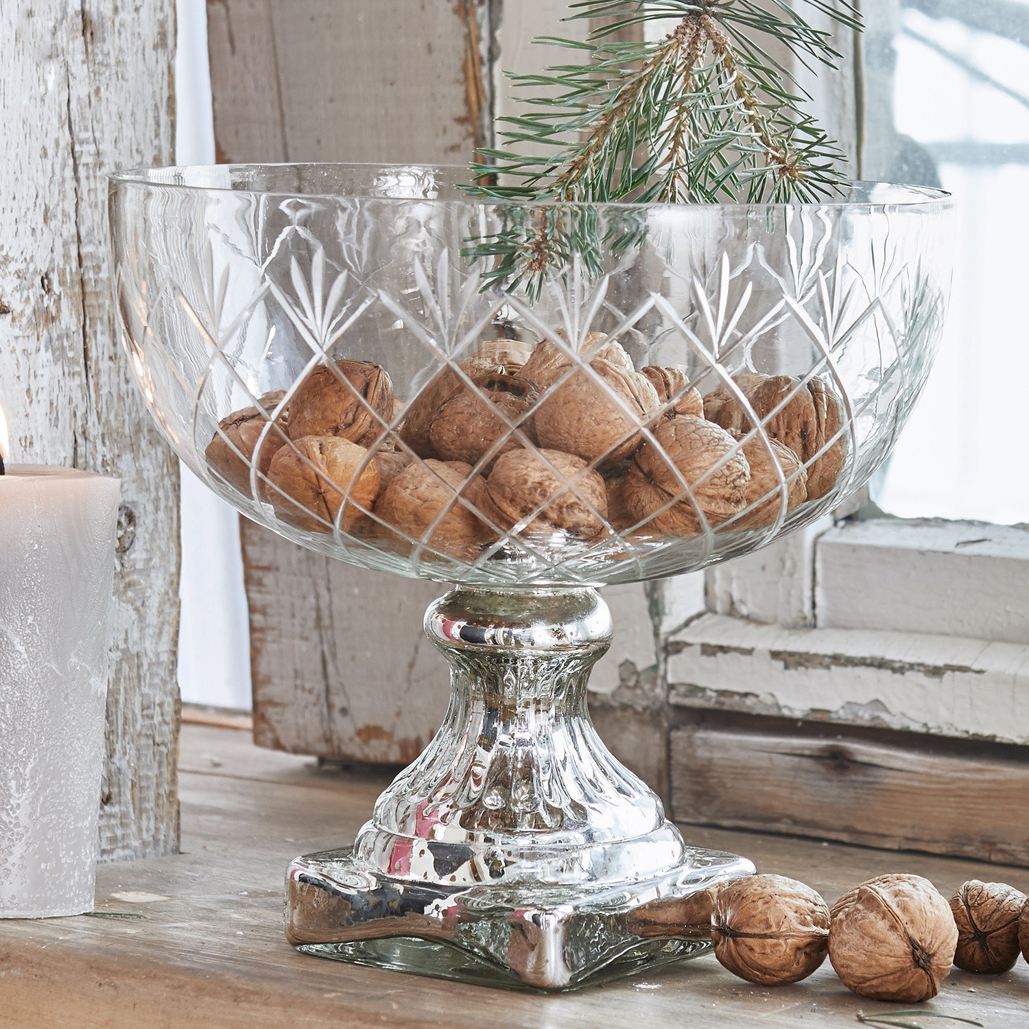 Coupe Iesha Coupe en verre sur pied avec base métallique argentée remplie de noix sur une table en bois rustique