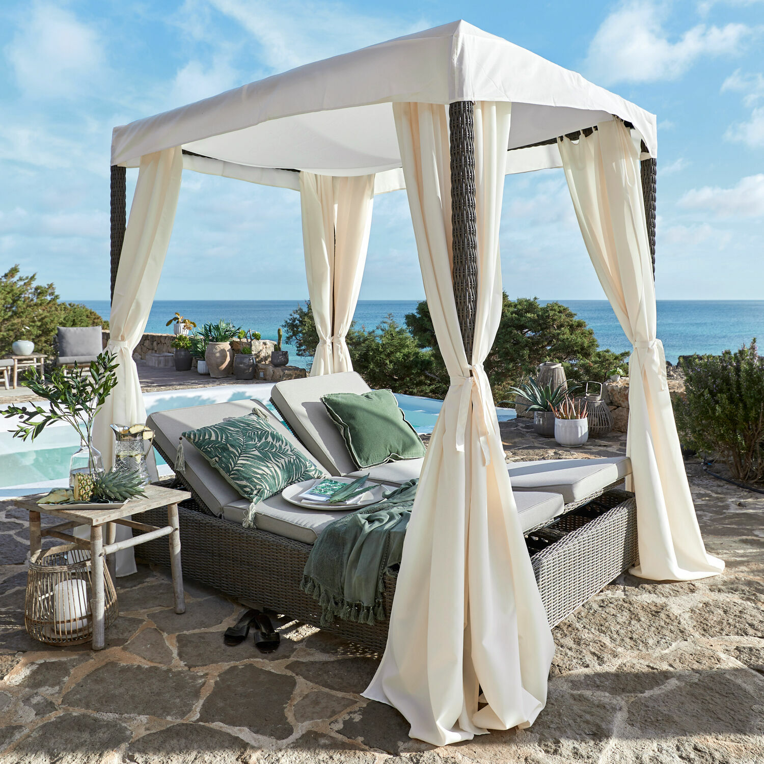 Canapé de jardin Hereford Chaise longue de jardin en rotin avec auvent crème sur terrasse en pierre face à la mer