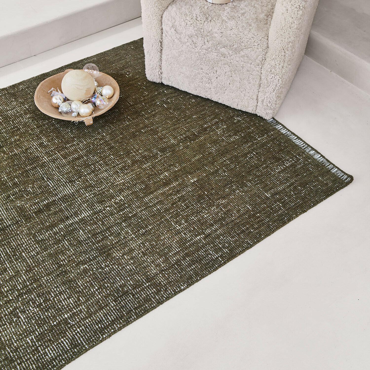 Tapis Shanira Tapis marron à motif subtil sur sol clair près d'un fauteuil crème avec décoration