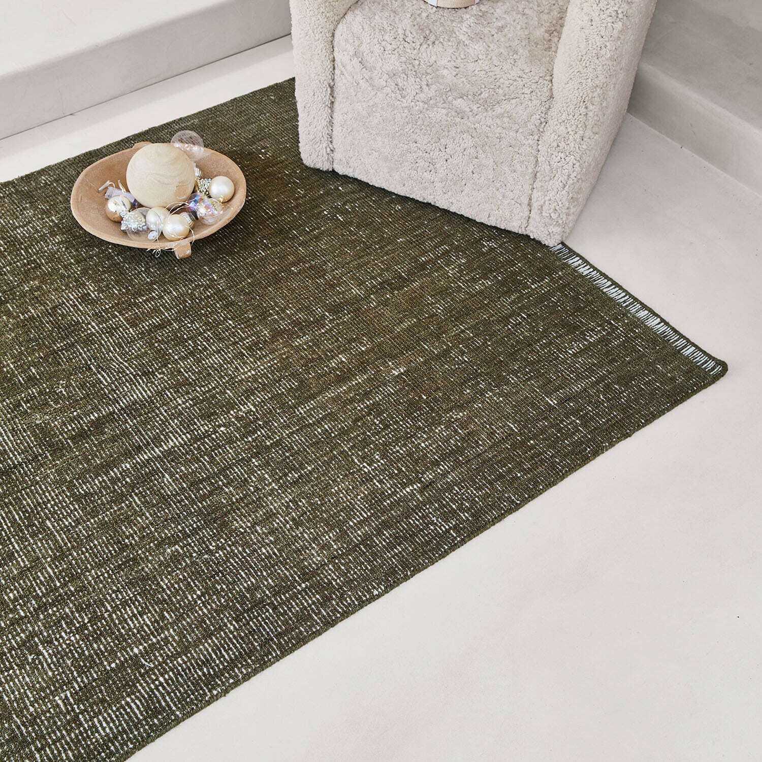 Tapis Shanira Tapis marron à motif subtil sur sol clair près d'un fauteuil crème avec décoration