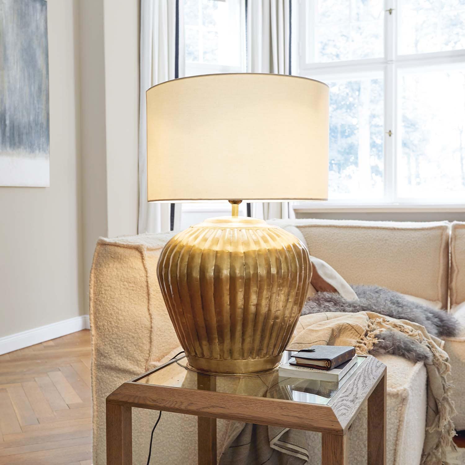 Lampe de table en laiton avec abat-jour beige sur une table en bois dans un salon lumineux