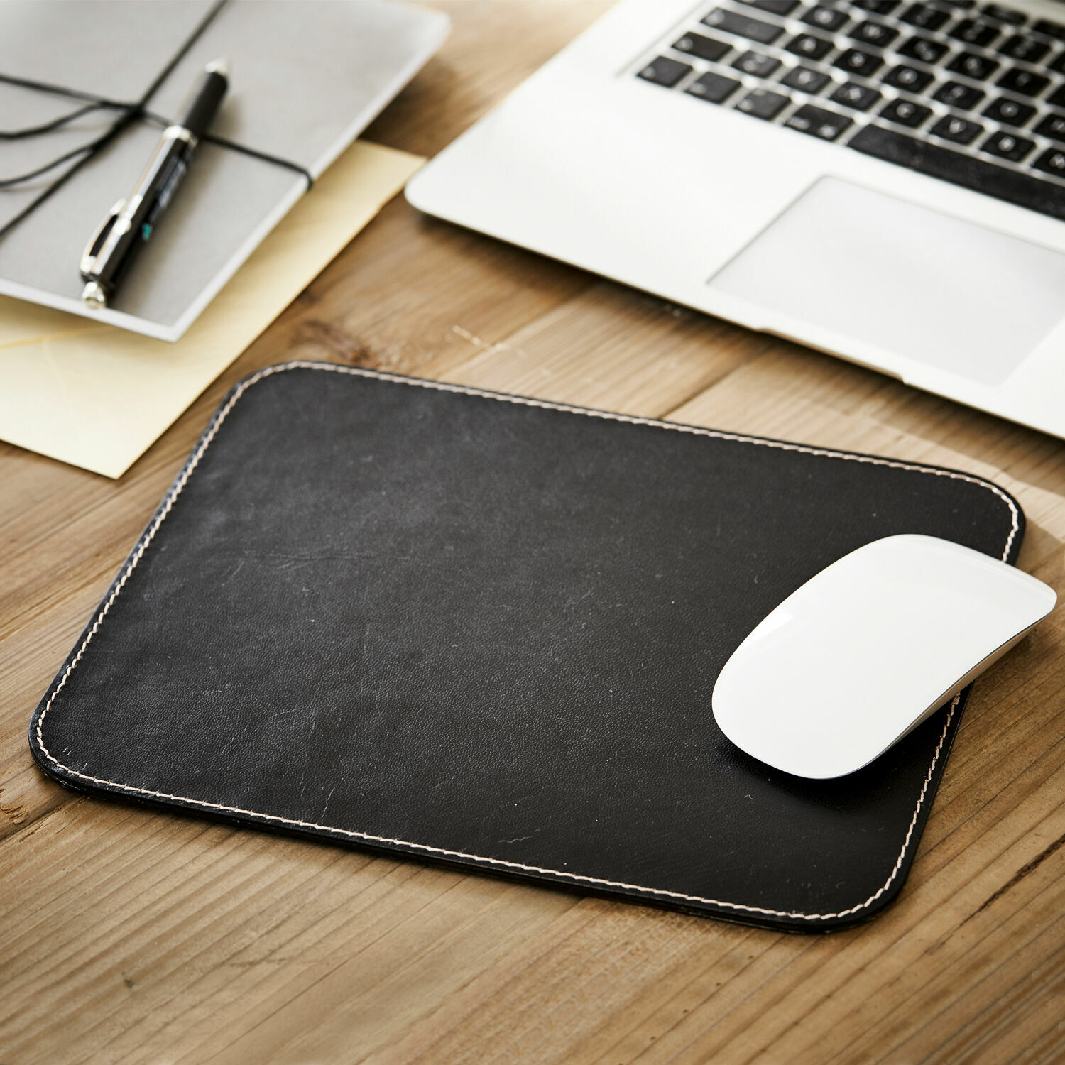Tapis de souris Dehaan Tapis de souris en cuir noir avec couture blanche sur bureau en bois à côté d'un ordinateur portable