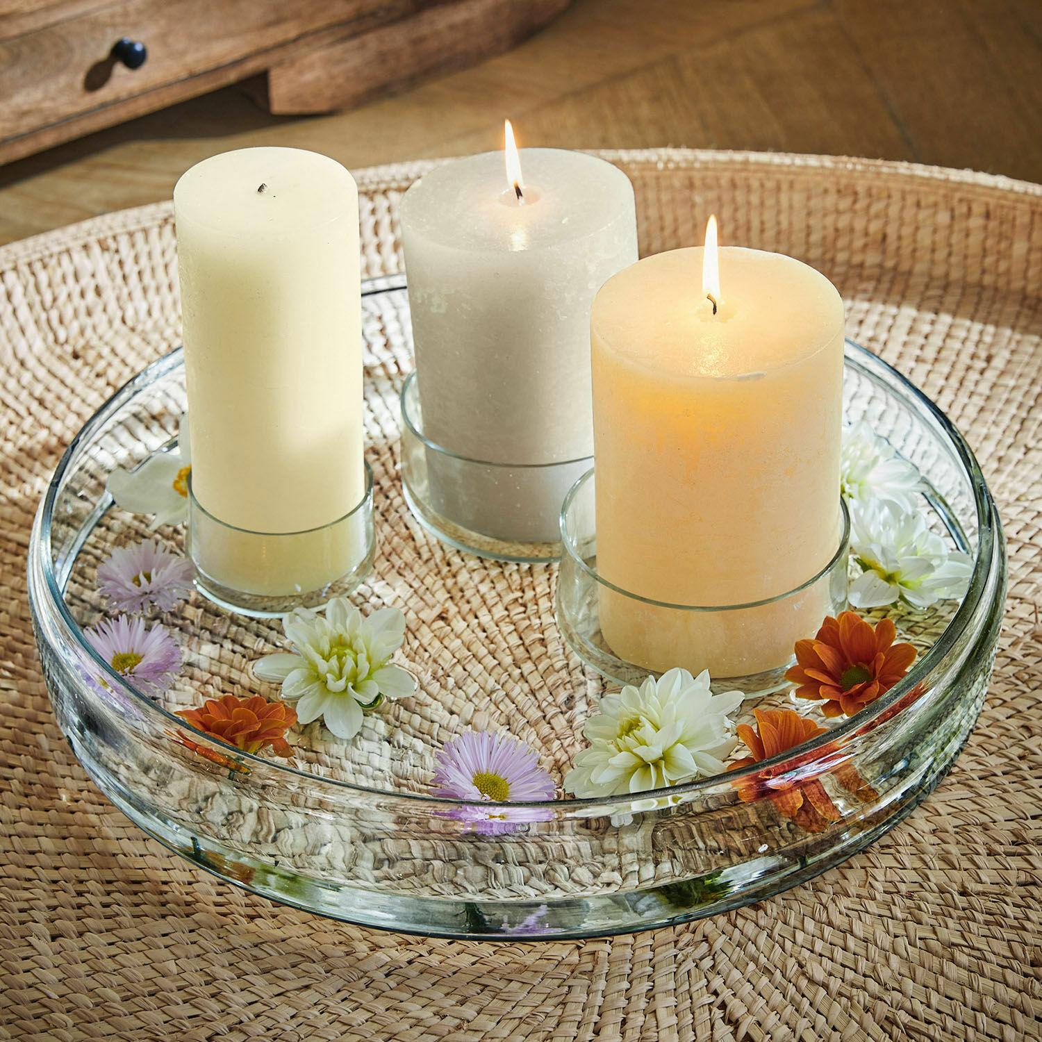 Support à bougies Marton Plateau en verre avec trois bougies pastel et fleurs sur table en osier tressé