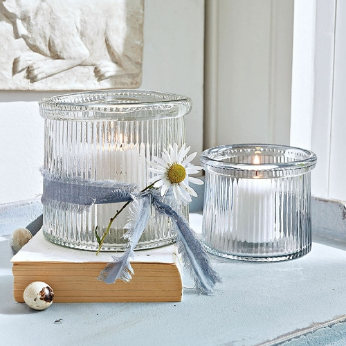 Photophores en verre cannelé avec bougies blanches et ruban décoratif avec fleur blanche.