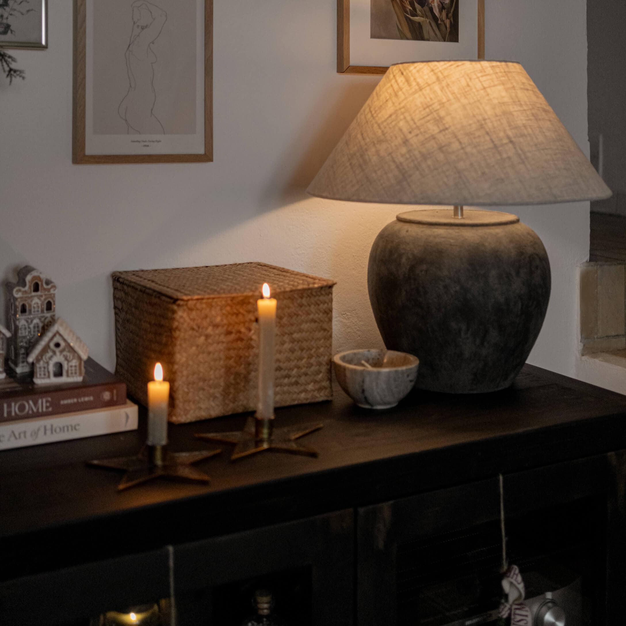 Lampe de table en céramique gris foncé avec abat-jour beige sur meuble sombre avec bougies et décorations