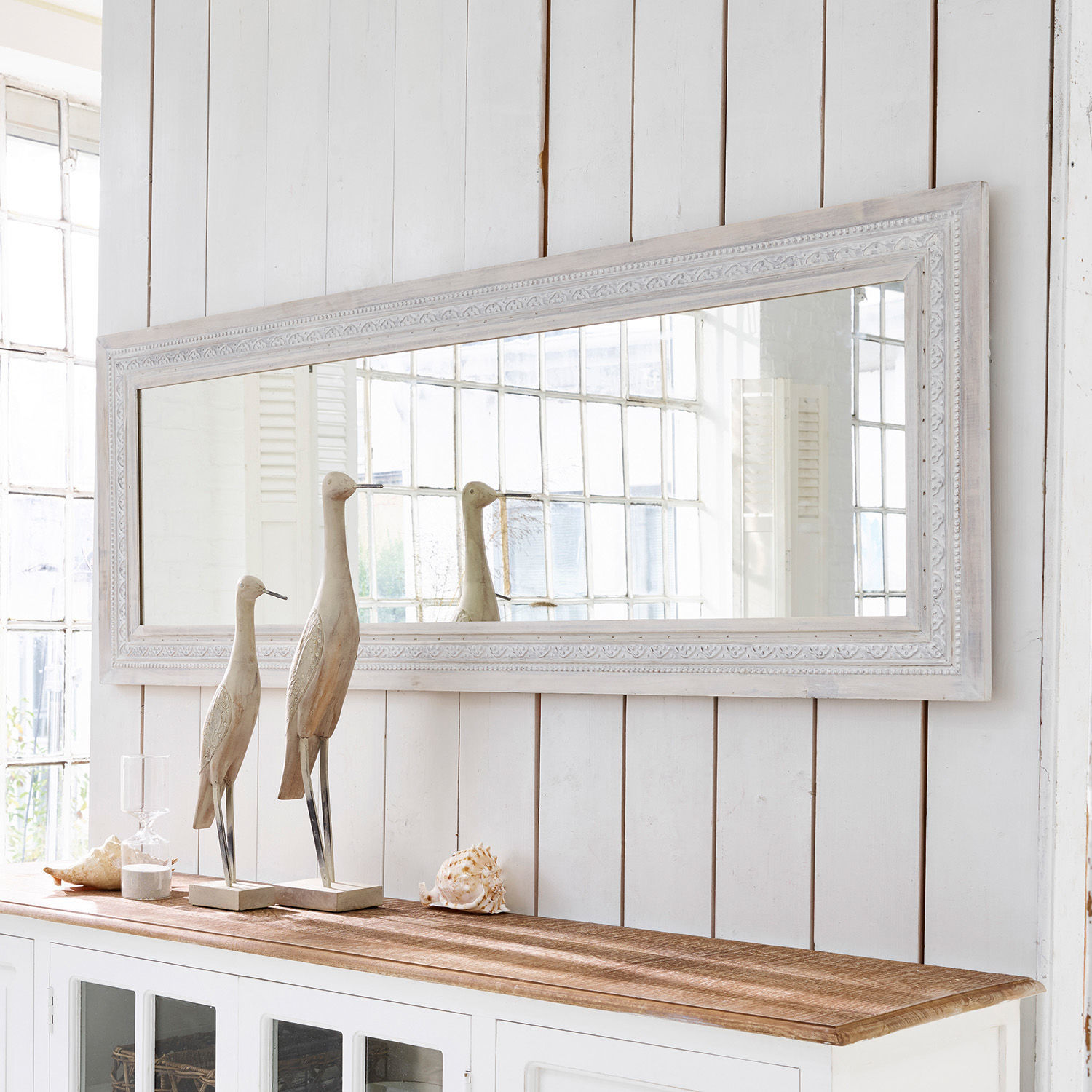 Miroir Milanu Grand miroir rectangulaire avec cadre en bois blanc au-dessus d'un buffet blanc décoré de sculptures en bois et coquillages