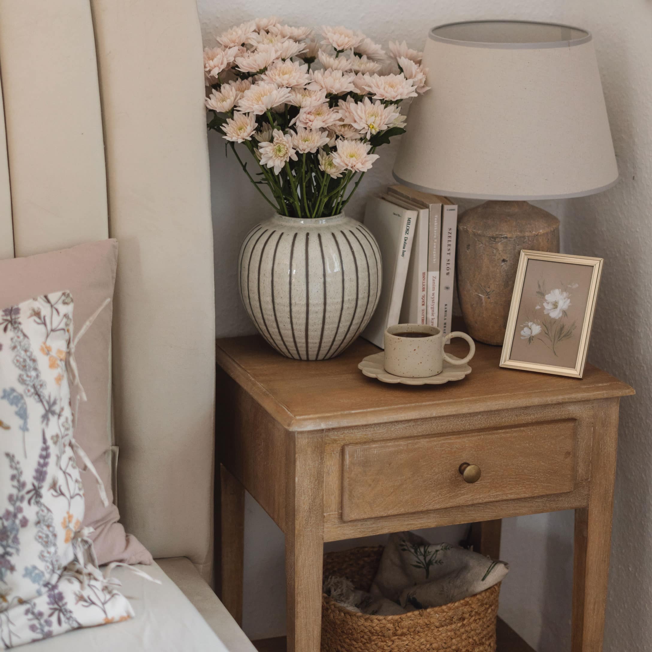 Table de chevet en bois avec lampe en céramique, vase et tasse de café dans une chambre chaleureuse