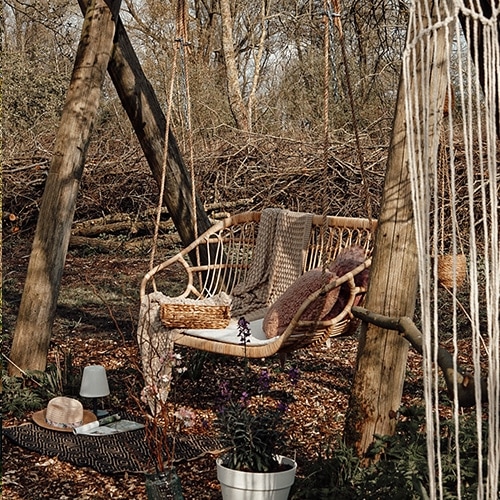 Balançoire de jardin en rotin naturel avec coussins et plaid dans un décor forestier automnal