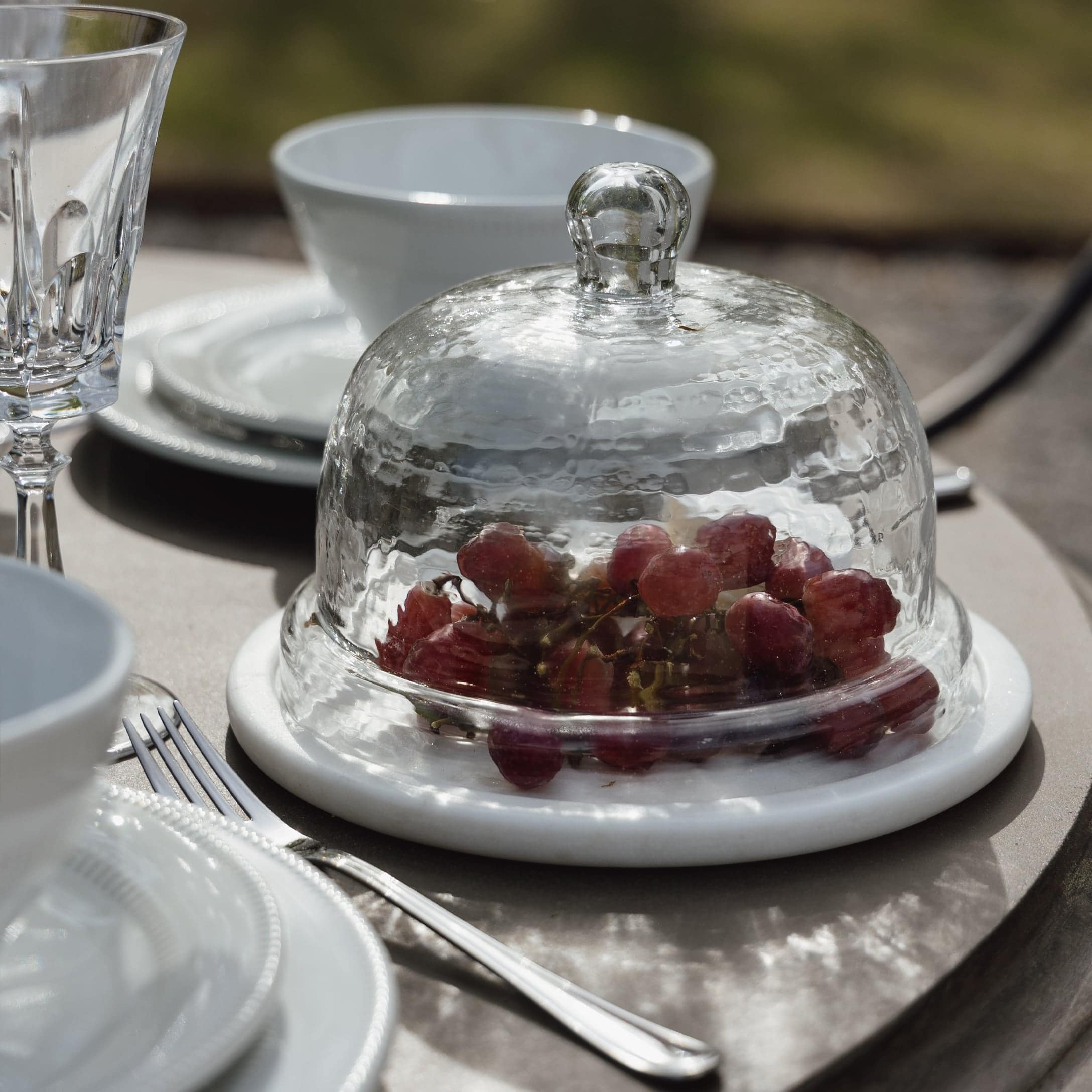Cloche en verre sur base en marbre blanc avec raisins rouges sur une table extérieure