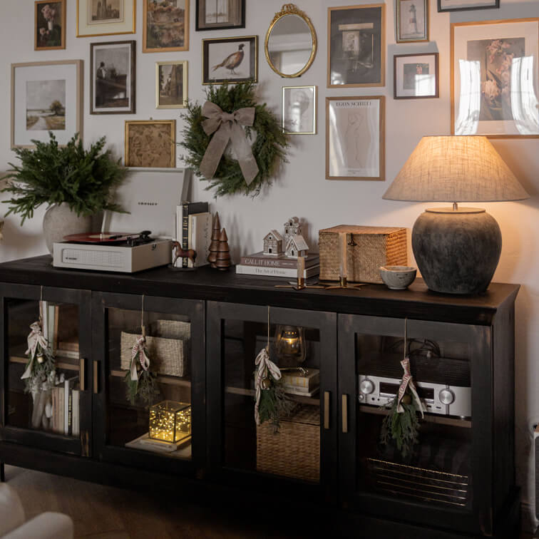 Buffet en bois noir avec portes vitrées, décorations de Noël et lampe en céramique dans un salon cosy