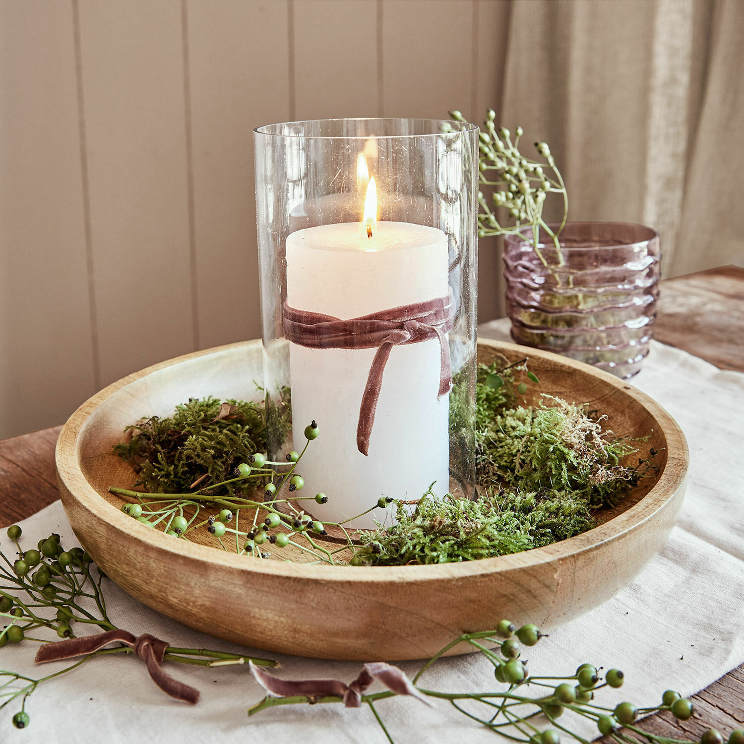 Bougie blanche dans un verre avec ruban en velours sur plateau en bois décoré de mousse verte