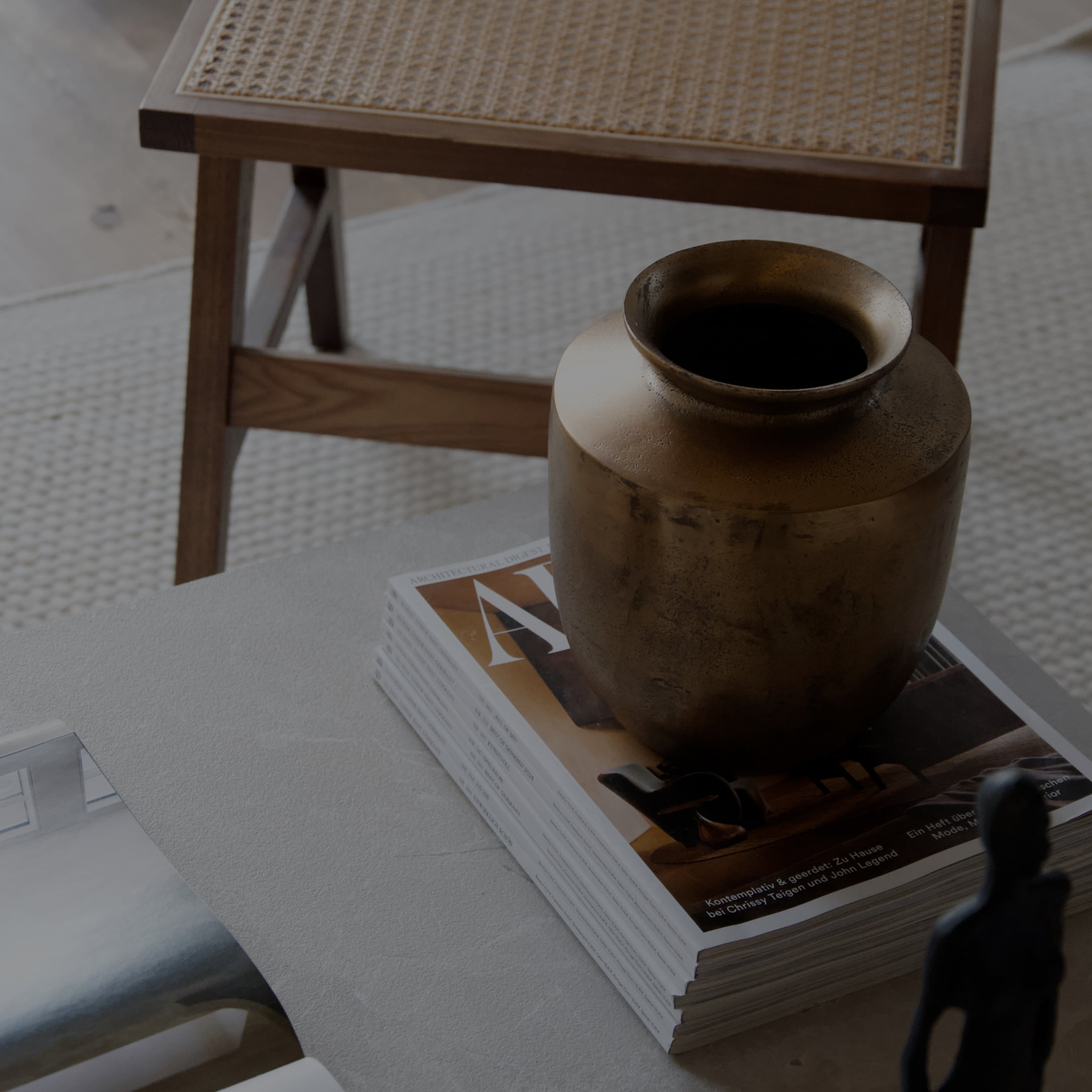 Vase décoratif en laiton posé sur une pile de magazines sur une table, bois naturel en arrière-plan