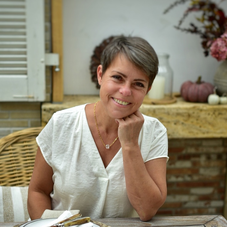 Femme souriante en chemise blanche assise à une table avec décorations automnales en arrière-plan