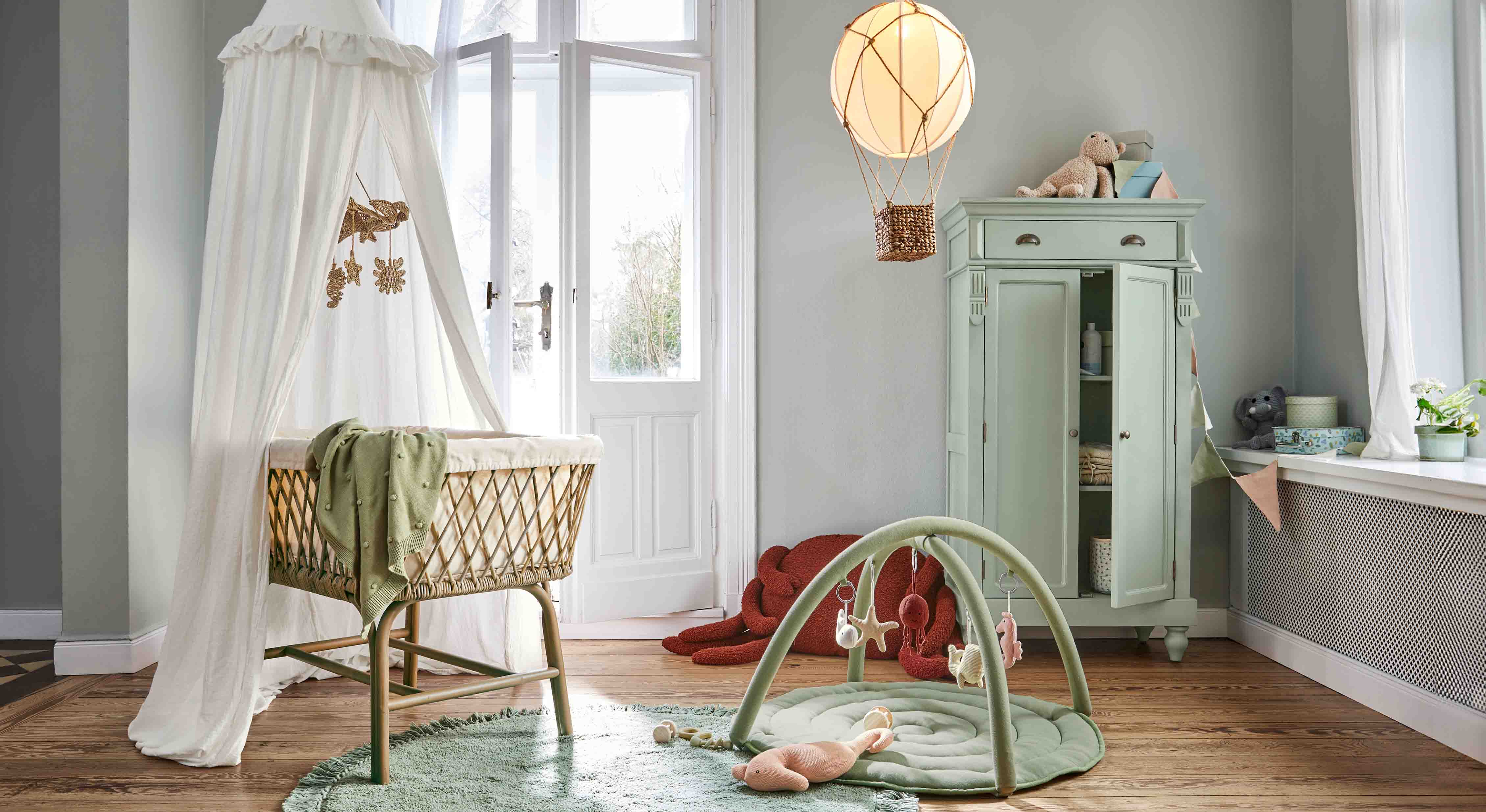 Chambre d'enfant chaleureuse avec berceau en osier, tapis vert et armoire pastel pour jouets et rangement