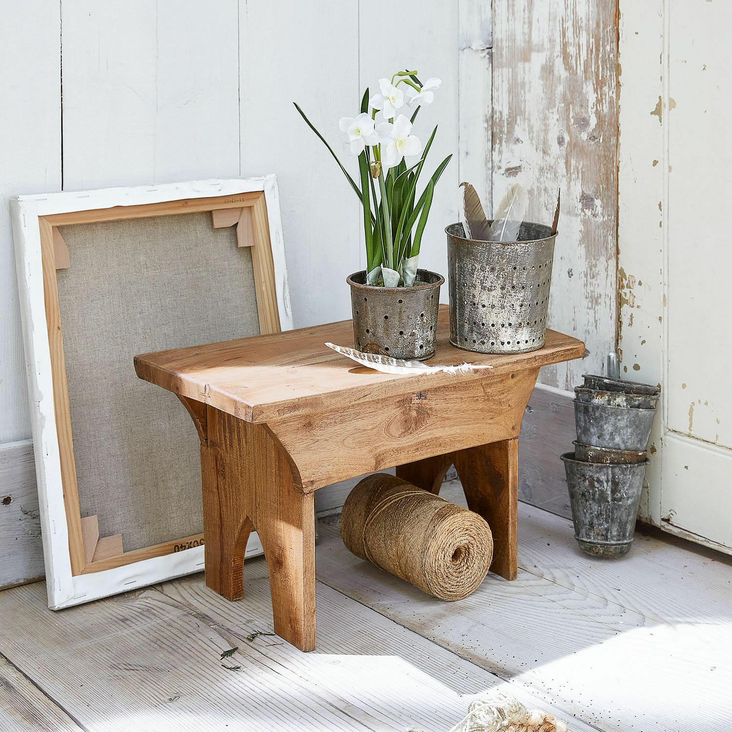 Tabouret Hoboken Petit tabouret en bois avec pots en métal et fleurs blanches sur un sol clair rustique