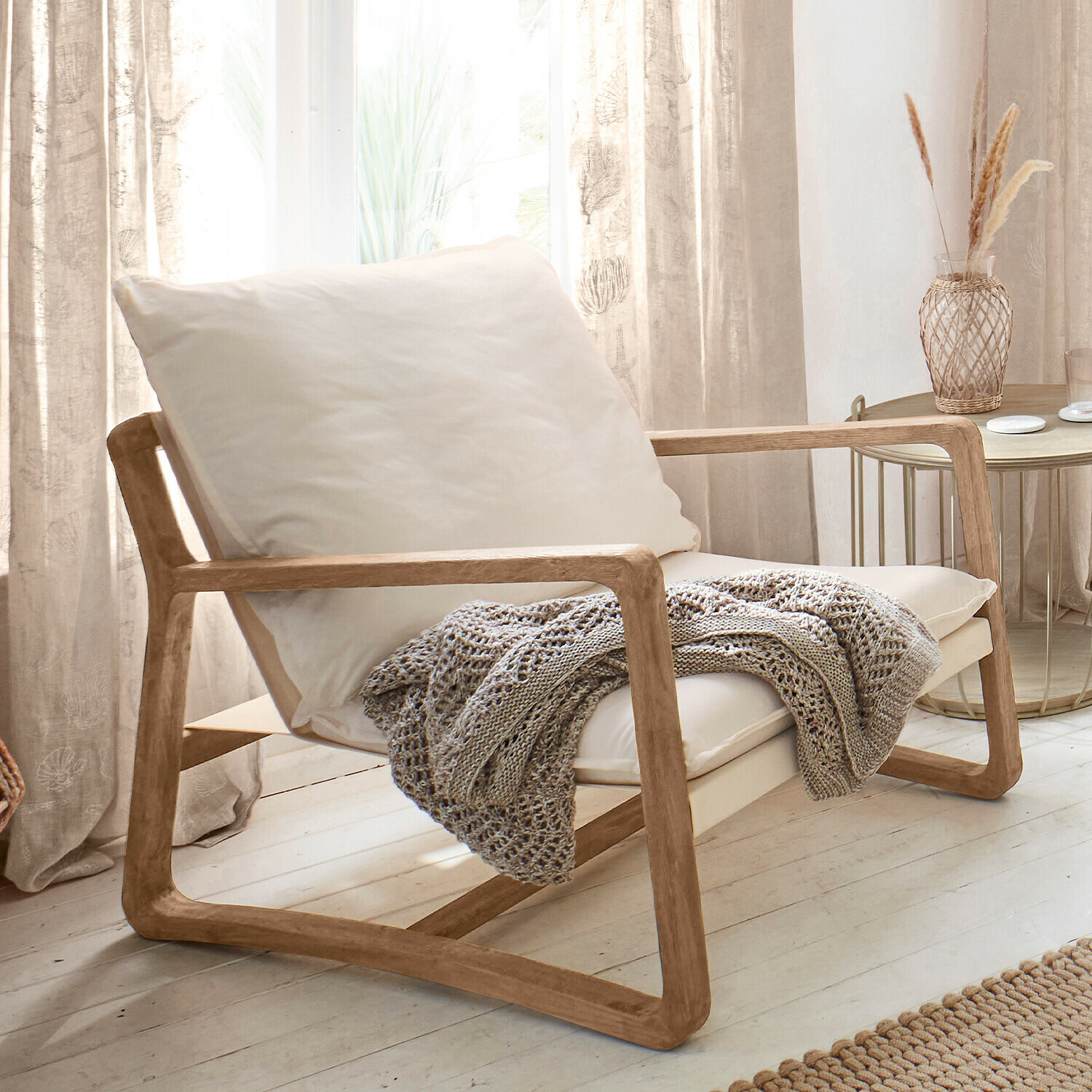 Fauteuil Jowna Fauteuil en bois clair avec coussin crème et plaid tricoté gris dans un salon lumineux