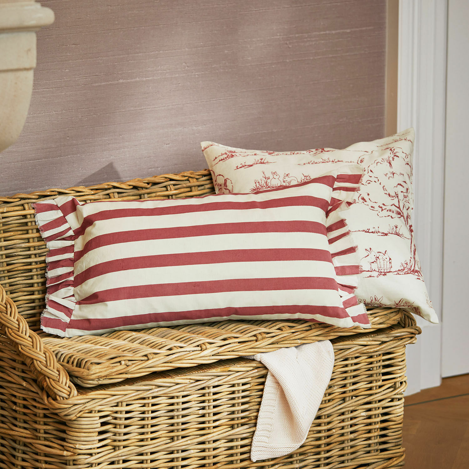 Lot de 2 housses de coussins Fleurine Deux coussins décoratifs en coton rayés rouge et blanc posés sur un banc en osier