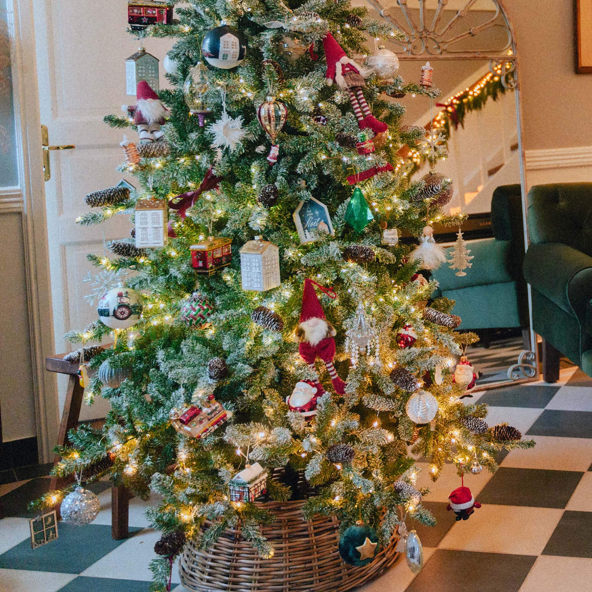 Sapin de Noël décoré avec lumières et ornements variés dans un panier en osier sur un sol à carreaux noir et blanc